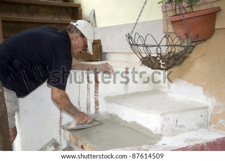 A senior man does cement work.  He is of Puerto Rican ethnicity.
