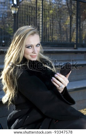 A Caucasian woman looks at camera while holding small mirror outdoors..