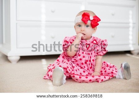 Six month old baby sits in red Valentine\'s day dress