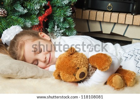 Little girl sleeping with teddy bear near christmas tree