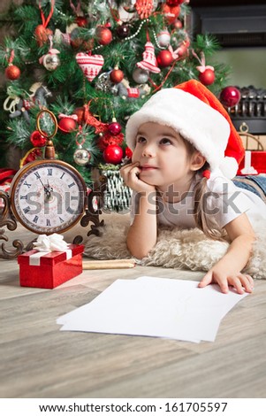 Little girl dreams about the gift and writes letter to Santa near christmas tree