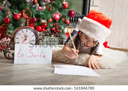 Happy girl in Santa hat writes letter to Santa Claus near christmas tree and clock