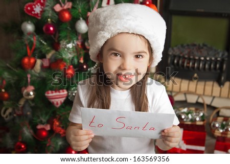 Smiling little girl in christmas hat holding letter for Santa