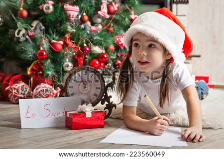 Thoughtful little girl in Santa hat writes letter to Santa Claus near christmas tree