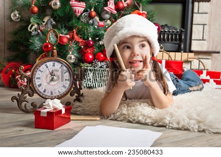 Dreaming little girl dreams about the gift and writes letter to Santa near christmas tree