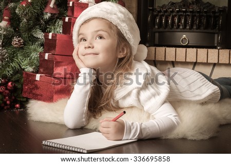 Pretty girl in Santa hat writes letter to Santa near christmas tree