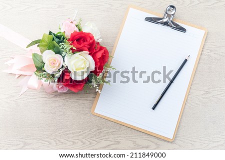 Wooden Clipboard attach planning paper with pencil on top beside rose bouquet on table