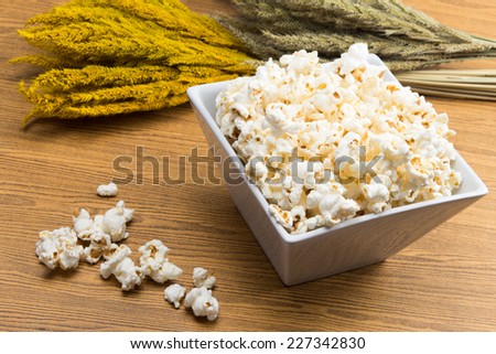 Popcorn in a square shape bowl with crop, rye beside on wood table