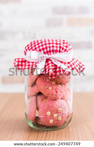 Strawberry cookies in glass canister, cap with plaid fabric, tied with a ribbon on wooden floor