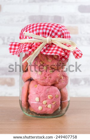Strawberry cookies in glass canister, cap with plaid fabric, tied with a ribbon on wooden floor