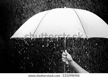 Hand holding an umbrella in rain, black background - business and fashion concept.