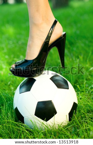 female\'s foot in black shoe with high heel standing on a soccer ball in green grass
