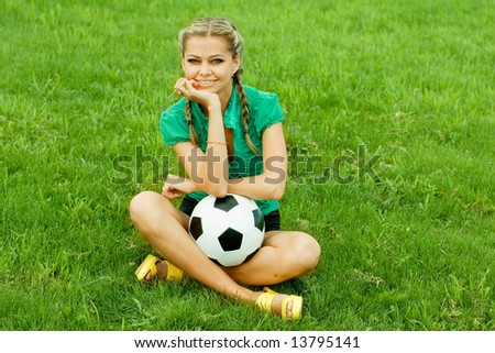 A girl sitting on a football field with a ball.