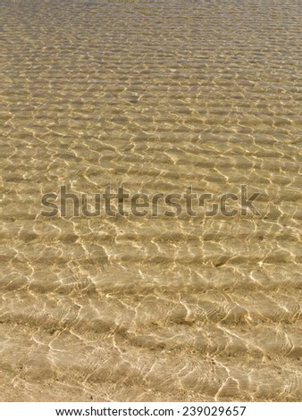 Sunlight plays in a transparent sea water and yellow sand strips