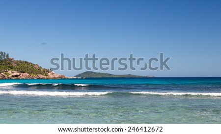 Bright panoramic seascape and marine turquoise waves with white foam rolls on the tropical coast of the island of La Digue, Seychelles