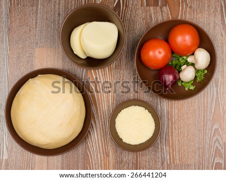 Ingredients for pizza: yeast dough, cheese, mozzarella, tomatoes, greens, mushrooms red onion on a dark wooden table
