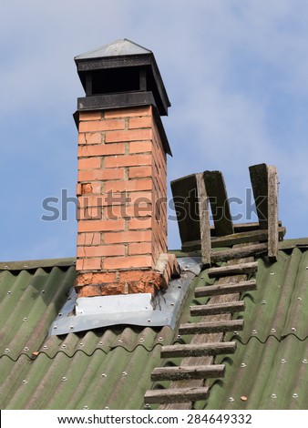 Old brick chimney with a headroom of stainless steel and wooden lnestnitsa on the green roof