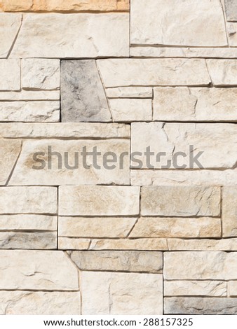 Wall artificial beige and gray marble stone with rough fractured surfaces, laid as a brick