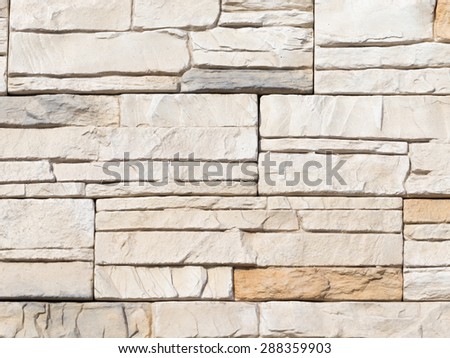 Wall artificial beige and gray cast stone with rough fractured surfaces, laid as a brick