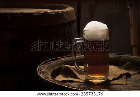 Two glasses of fresh foamy beer on a table in a vintage beer cellar with a barrel in the background