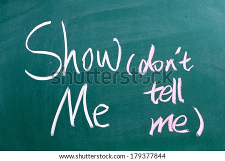 The phrase Show Me, Don\'t Tell Me written by hand in white chalk on a used blackboard. Often used in business but more so as a guide for novel and book writers