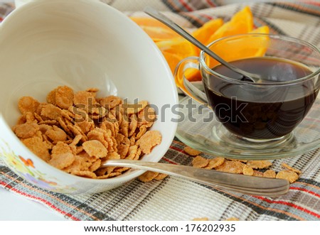 Flakes in a deep plate, cup of coffee and orange, sliced