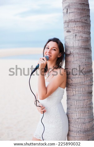 beautiful young girl singing into a microphone on the beach near the sea