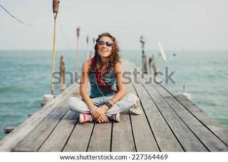 beautiful girl in sunglasses sitting on the sea pier looking into the distance and listening to pleasant music