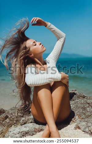 beautiful blonde girl with long hair posing on the beach in a white t-shirt and closed eyes