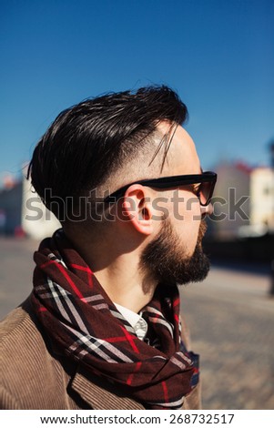 young man with beard and sunglasses posing on the street in the scarf