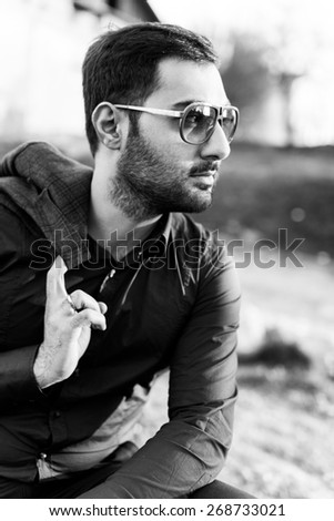 young man with beard and sunglasses posing on the street with a jacket in his hands