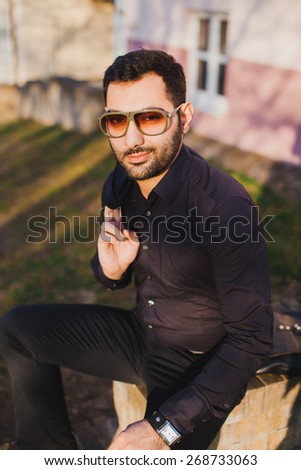 young man with beard and sunglasses posing on the street with a jacket in his hands