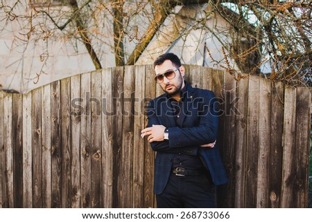 young man with beard and sunglasses posing on the street and Smoking a cigarette