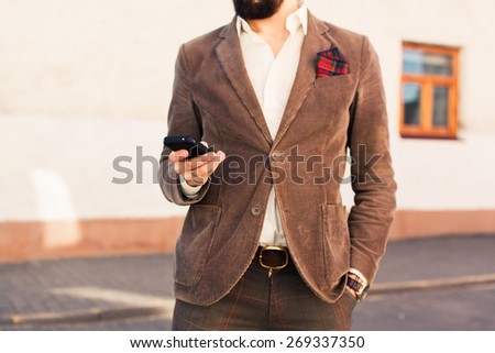 brutal man with a mustache and beard with a fashionable haircut posing on the street in a brown suit and talking on the phone