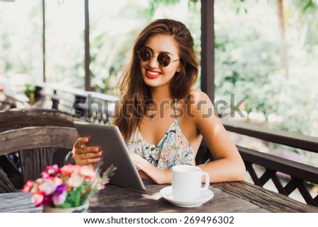 beautiful young woman in sunglasses sitting in a cafe drinking coffee/tea and work on your tablet on the Internet