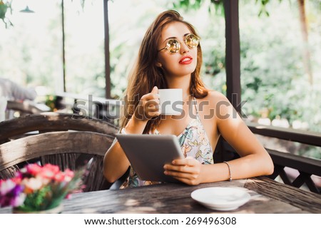 beautiful young woman in sunglasses sitting in a cafe drinking coffee/tea and work on your tablet on the Internet
