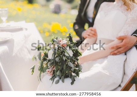 the bride and groom sit at the table in the hands of the bride a bouquet of wildflowers and roses