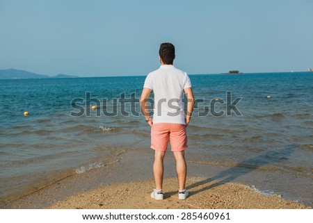 young guy in a white t-shirt and sunglasses stands back and looks at sea