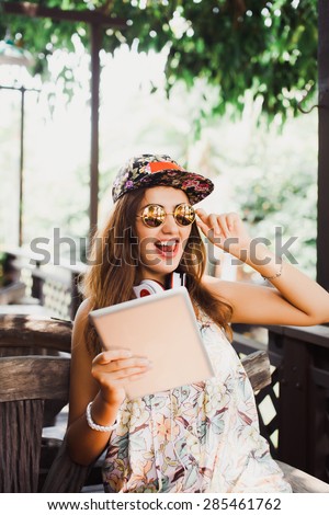 young girl in sunglasses and a cap works on a tablet sitting in a cafe
