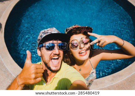 beautiful loving couple in bright sun glasses and caps baseball caps make selfi on the background of the pool
