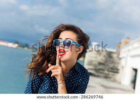young girp in sunglasses with red lips and hair posing in the pier