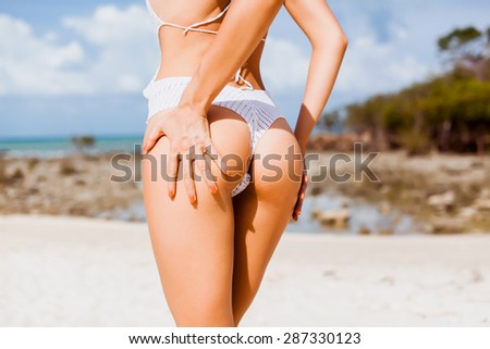 beautiful young woman in white bikini posing on a rocky seaside in turning booty shows ass