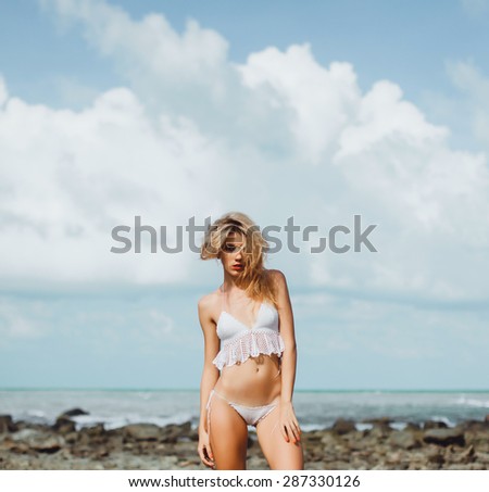 beautiful young woman in white bikini posing on a rocky seaside