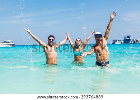 friends standing in bikinis and sunglasses at sea happy hands up in the air victoriously happy