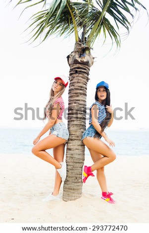 beautiful girl friend in sneakers, shorts and t-shirts posing near palm trees in caps baseball caps
