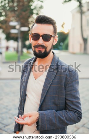 young guy with a beard and mustache with sunglasses and jacket posing on the street the sun shines