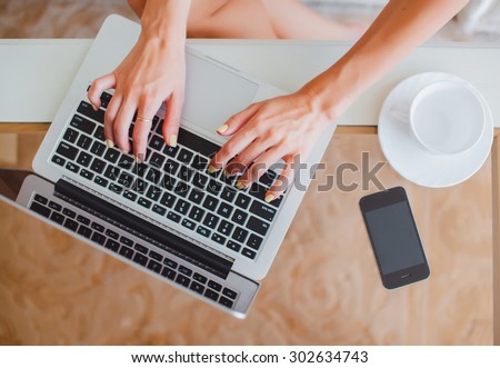 young girl woman working on a laptop sitting at home write messages to drinking coffee smiling typing on a keyboard