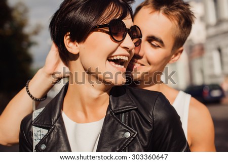 Young handsome stylish guy listing her pretty blonde girlfriend, romantic sensual couple hugs on the street of european city at bright evening sunlight rock n roll styled clothes and sunglasses couple