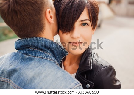 Fashion outdoor sensual romantic portrait of beautiful young couple hugs and kissing on the stereo of european city. Wearing trendy fall black outfits, rock n roll style. Bright evening sunlight.