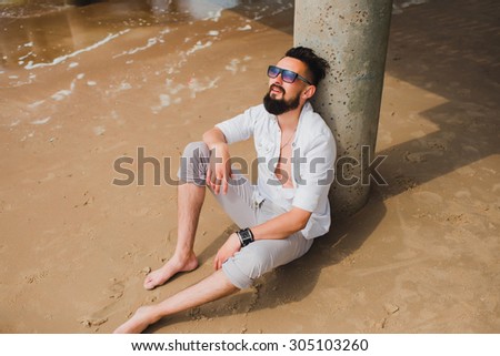 Outdoor lifestyle coolest portrait of brutal,tattooed man,posing at California beach,tattoos,denim jeans sunglasses.west coast,Florida beach,Hipster man on the beach